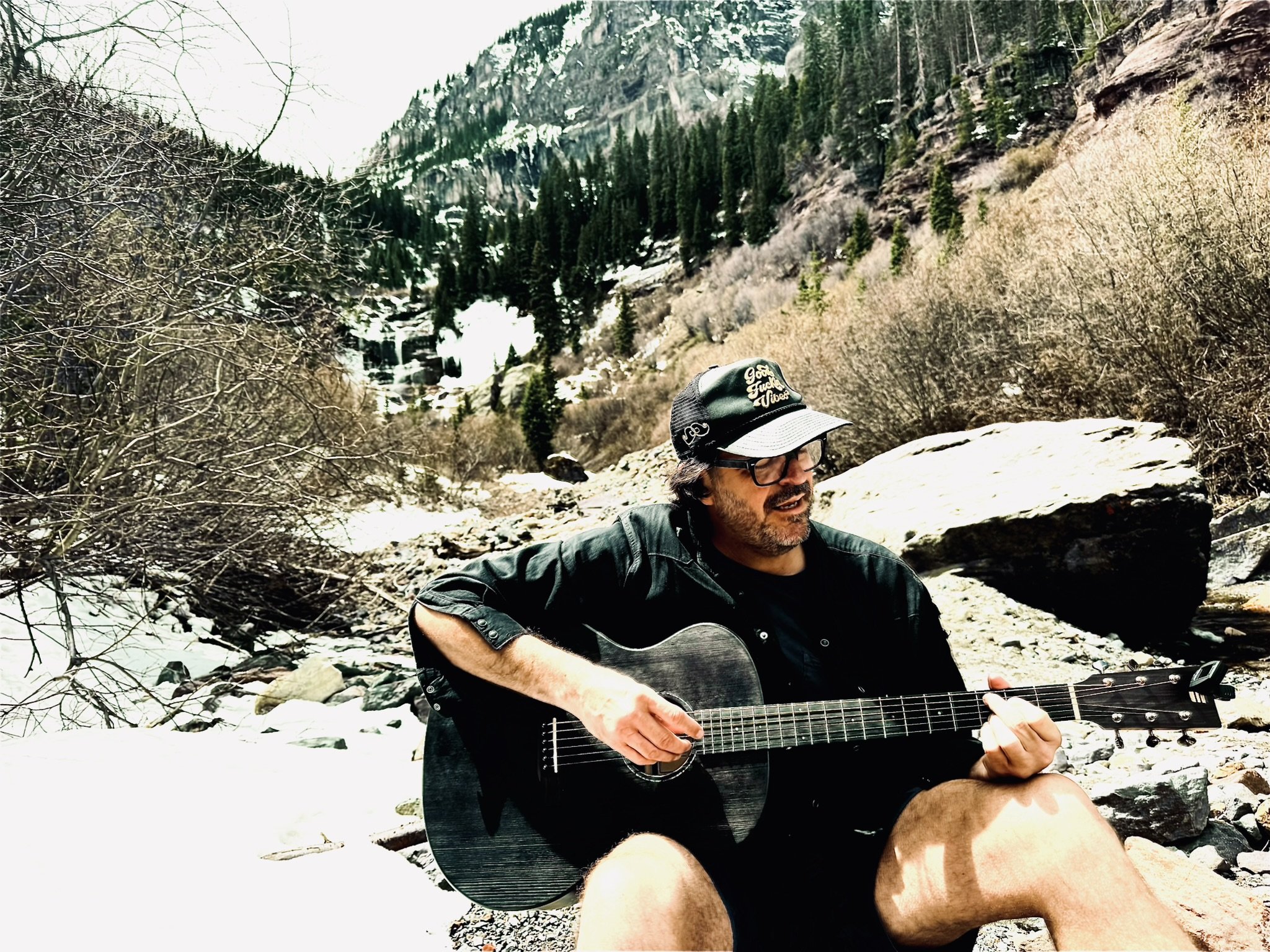 Dustin playing guitar beside a mountain creek